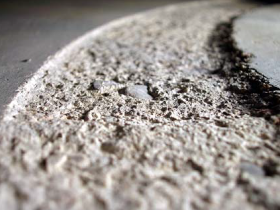 An abrasion test has worn a groove in the concrete slab, showing the aggregate underneath the paste.